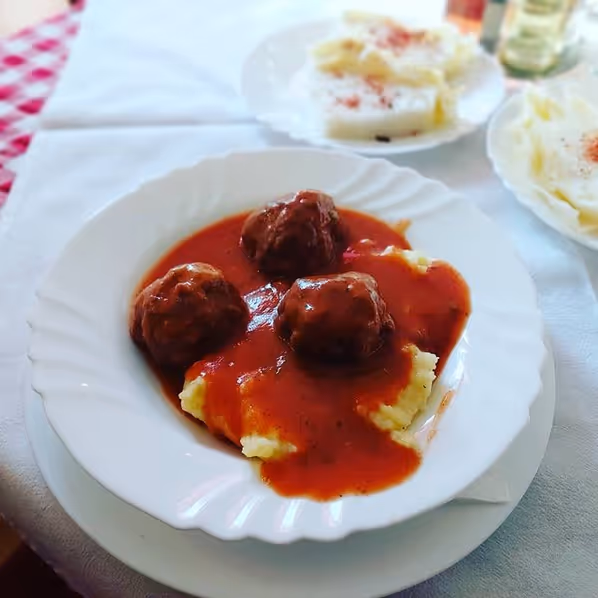 Plate of meatballs served over mashed potatoes with red tomato sauce on a white tablecloth.